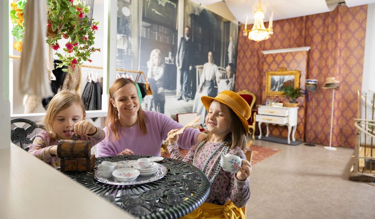 Äiti ja kaksi tyttöä leikkimässä teekutsuja kahvilan pöydän ääressä.