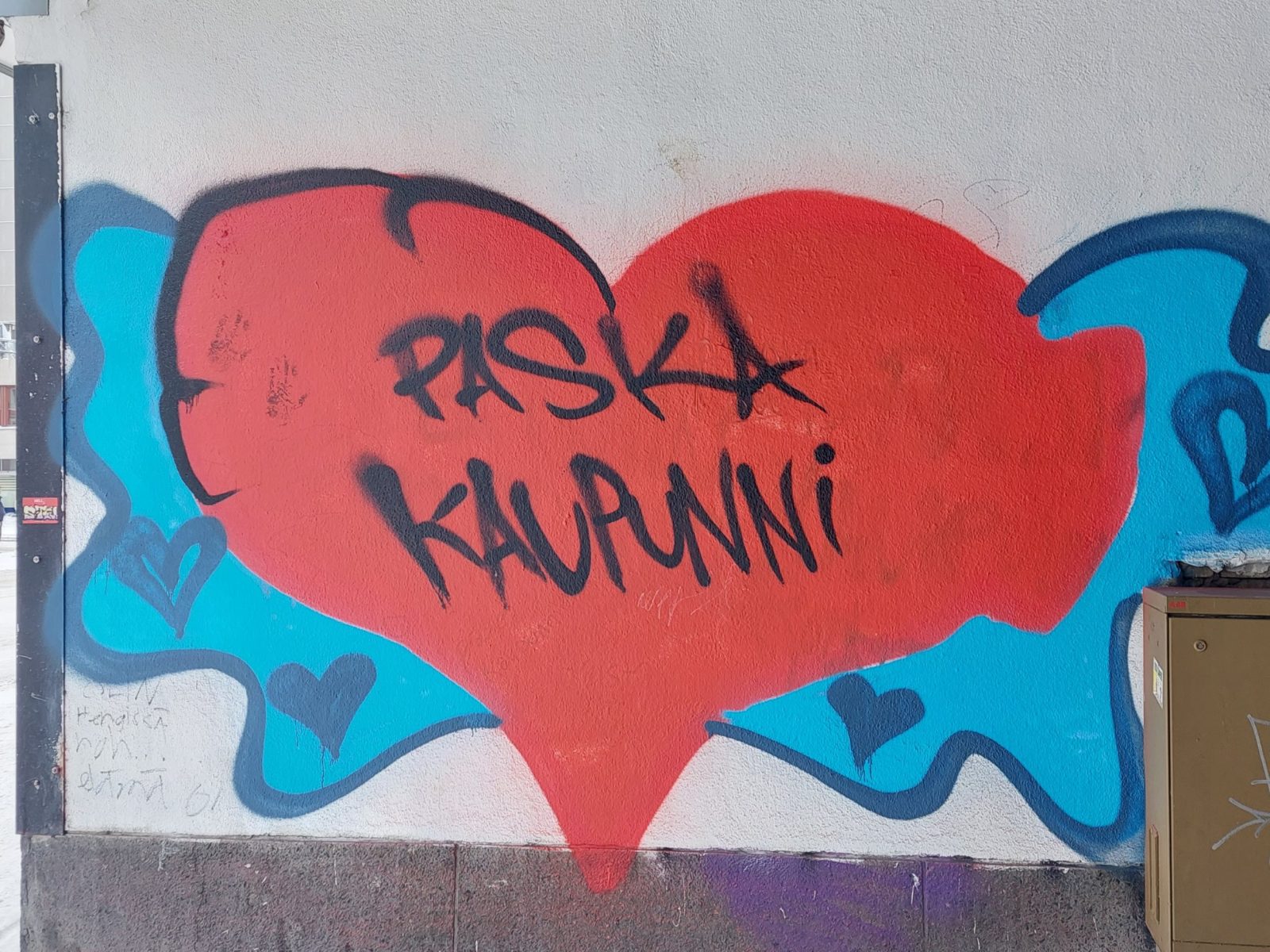 Graffiti: Paska kaupunni. Tekstin ympärillä iso punainen sydän sekä sinistä taustaväriä.