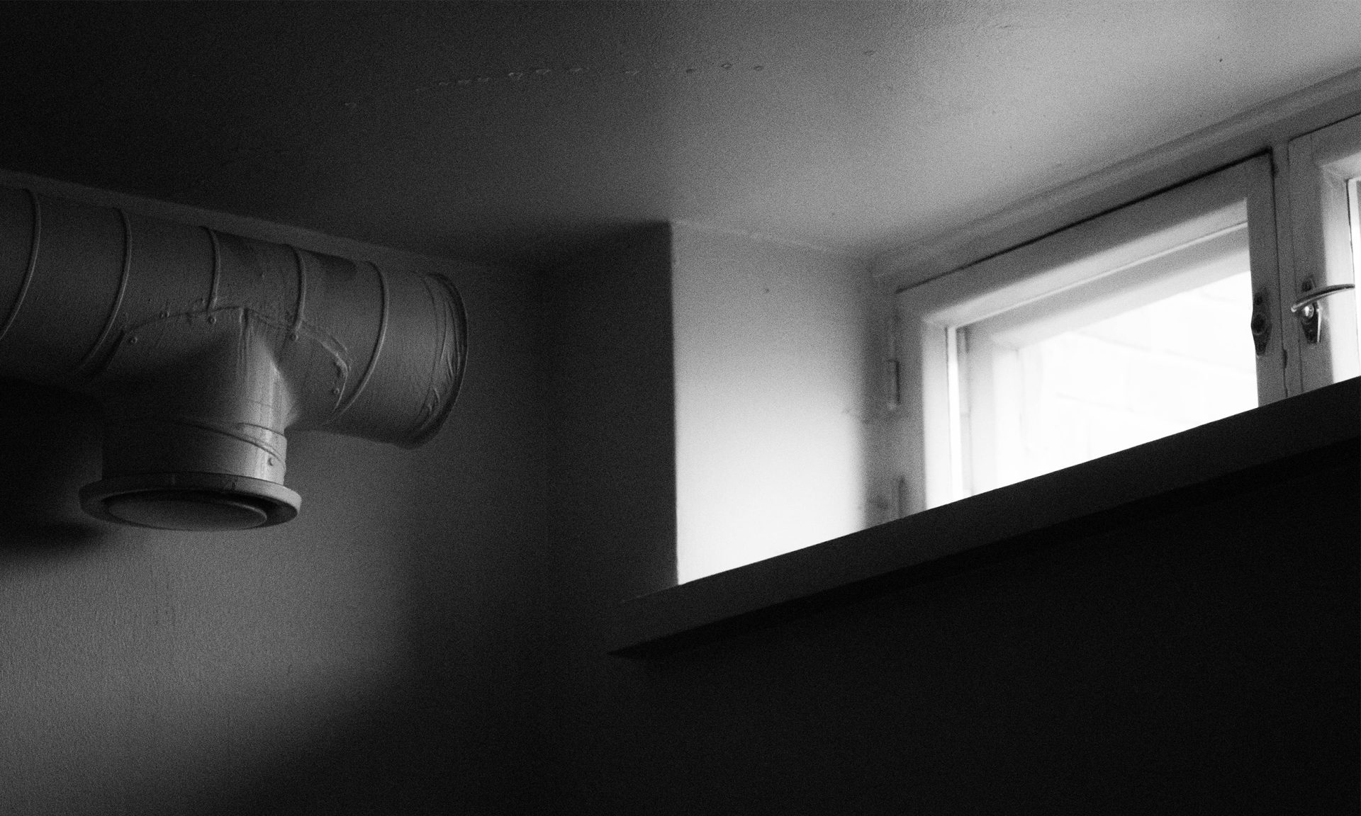 Black and white picture of a basement room. Window in the right upper corner. On the left an air vent.