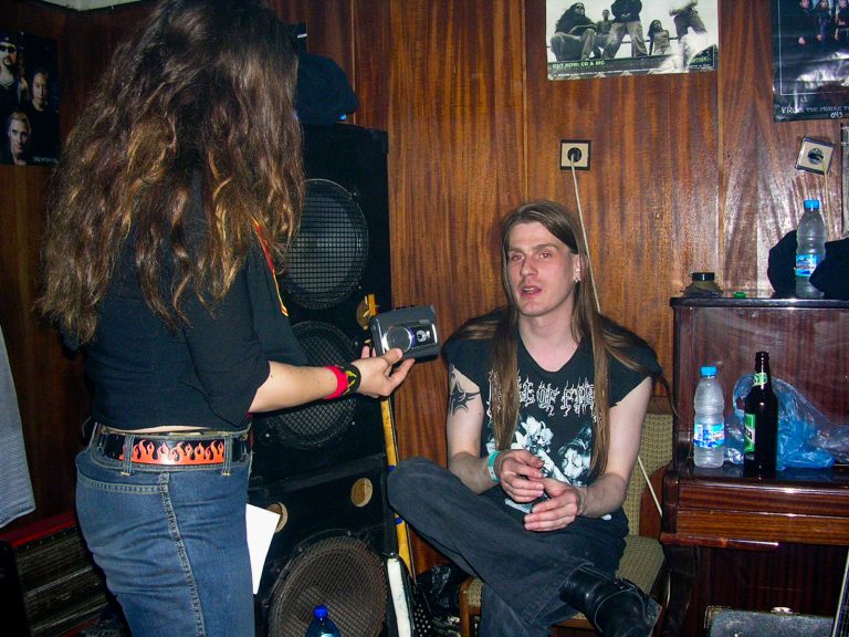 Riku Hopeakoski is sitting and talking while the interviewer stands and records the conversation.