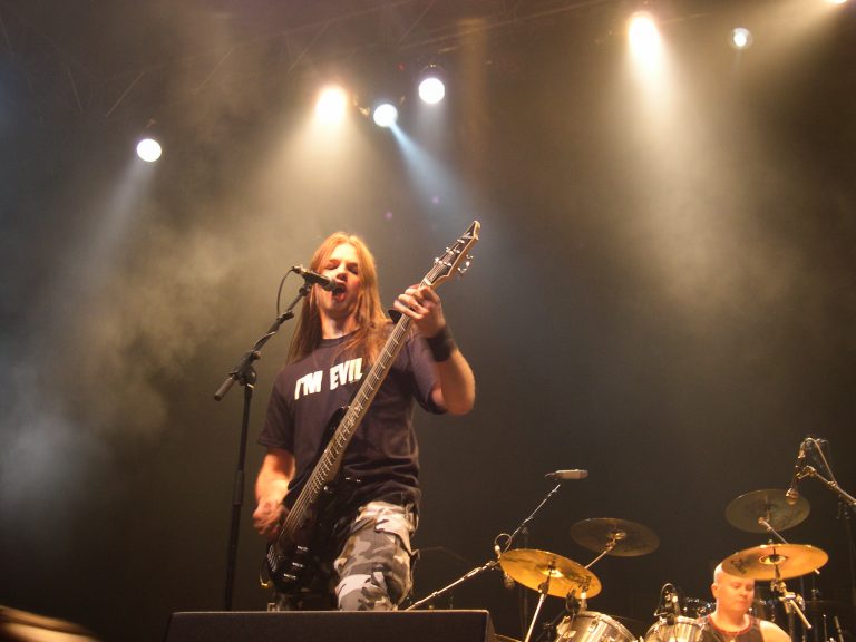 On the concert stage under the spotlights, vocalist-bassist Altti Veteläinen stands in the foreground. In the background, the drums and drummer are visible.