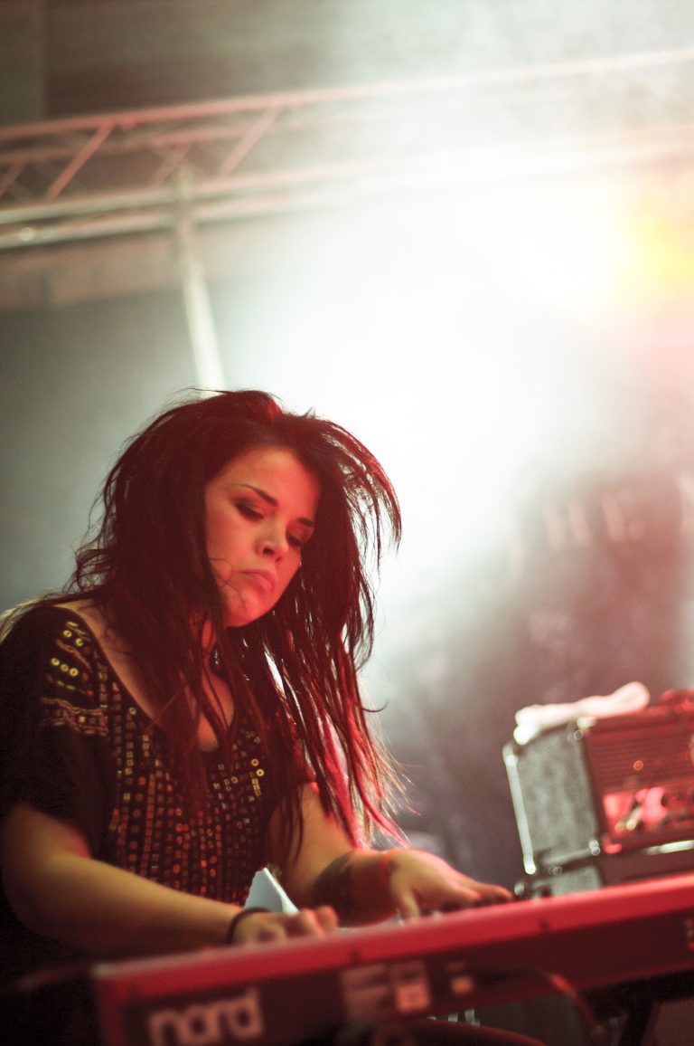 The keyboardist is focused, eyes on the keys. Bright stage lights shine in the background.